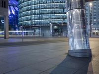 an empty city street at night as a cyclist passes by a tall building lit up in blue light