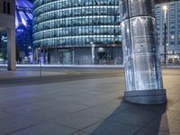 an empty city street at night as a cyclist passes by a tall building lit up in blue light