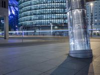 an empty city street at night as a cyclist passes by a tall building lit up in blue light