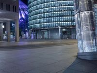 an empty city street at night as a cyclist passes by a tall building lit up in blue light