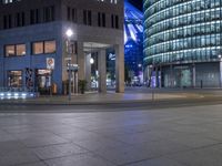 an empty city street at night as a cyclist passes by a tall building lit up in blue light