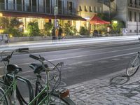 two bicycles are parked along a street next to a sidewalk in front of buildings with tables on both sides of them