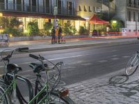 two bicycles are parked along a street next to a sidewalk in front of buildings with tables on both sides of them