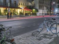 two bicycles are parked along a street next to a sidewalk in front of buildings with tables on both sides of them