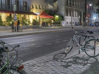 two bicycles are parked along a street next to a sidewalk in front of buildings with tables on both sides of them