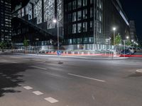 a road in front of tall buildings with lights on at night time in an urban area