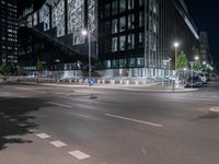 a road in front of tall buildings with lights on at night time in an urban area