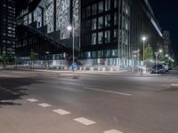 a road in front of tall buildings with lights on at night time in an urban area