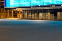 a blue lit building sits by a closed street, with an empty sidewalk at night