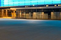 a blue lit building sits by a closed street, with an empty sidewalk at night