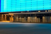 a blue lit building sits by a closed street, with an empty sidewalk at night