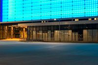 a blue lit building sits by a closed street, with an empty sidewalk at night