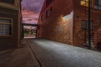 an empty narrow alley with street lights lit up at night in the distance are brick buildings