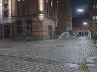 a brick street with a bridge at night near buildings on either side of it with lights on