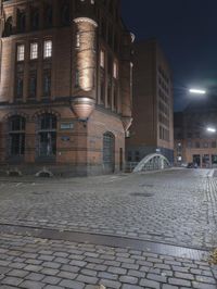 a brick street with a bridge at night near buildings on either side of it with lights on