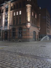 a brick street with a bridge at night near buildings on either side of it with lights on