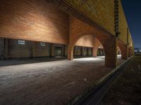 an empty brick building with arches and lighting underneath it at night time in the city