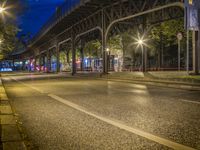 a bridge spans over an empty city street at night by trees and benches along the sidewalk