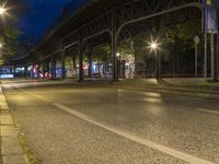 a bridge spans over an empty city street at night by trees and benches along the sidewalk