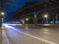 a bridge spans over an empty city street at night by trees and benches along the sidewalk