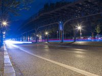 a bridge spans over an empty city street at night by trees and benches along the sidewalk