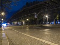 a bridge spans over an empty city street at night by trees and benches along the sidewalk