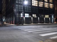 a building on a street corner with cross walk lights over the street at night, and people walking down the street