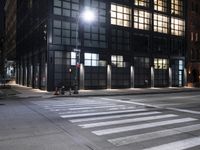 a building on a street corner with cross walk lights over the street at night, and people walking down the street