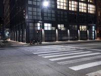 a building on a street corner with cross walk lights over the street at night, and people walking down the street