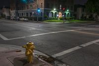 a fire hydrant sits on the sidewalk at night by a busy street corner with a building and cars