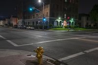 a fire hydrant sits on the sidewalk at night by a busy street corner with a building and cars