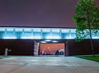 the front entrance to a building at night, with people sitting under an umbrella on a patio