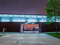 the front entrance to a building at night, with people sitting under an umbrella on a patio