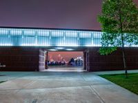 the front entrance to a building at night, with people sitting under an umbrella on a patio