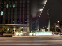 a view of a city intersection at night time, with a street light on a walkway beside the building