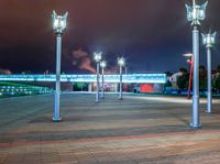 a night scene showing several street lights in a plaza with a bridge and clouds behind