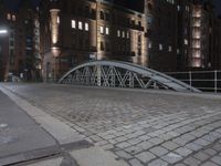 a sidewalk is lit by a bridge with cobblestone pavement outside of it at night