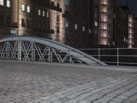 a sidewalk is lit by a bridge with cobblestone pavement outside of it at night
