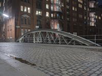 a sidewalk is lit by a bridge with cobblestone pavement outside of it at night