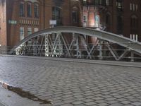 a sidewalk is lit by a bridge with cobblestone pavement outside of it at night
