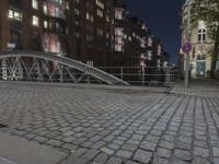 a sidewalk is lit by a bridge with cobblestone pavement outside of it at night