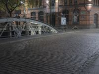 a sidewalk is lit by a bridge with cobblestone pavement outside of it at night