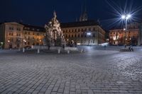 an old cobblestone plaza at night with two statues and a statue in the background