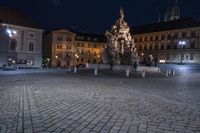 an old cobblestone plaza at night with two statues and a statue in the background