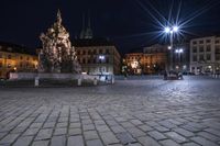 an old cobblestone plaza at night with two statues and a statue in the background