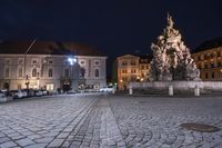 an old cobblestone plaza at night with two statues and a statue in the background