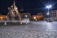 an old cobblestone plaza at night with two statues and a statue in the background