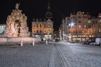 an old cobblestone plaza at night with two statues and a statue in the background