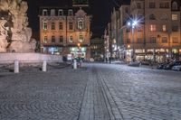 an old cobblestone plaza at night with two statues and a statue in the background