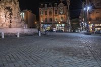 an old cobblestone plaza at night with two statues and a statue in the background